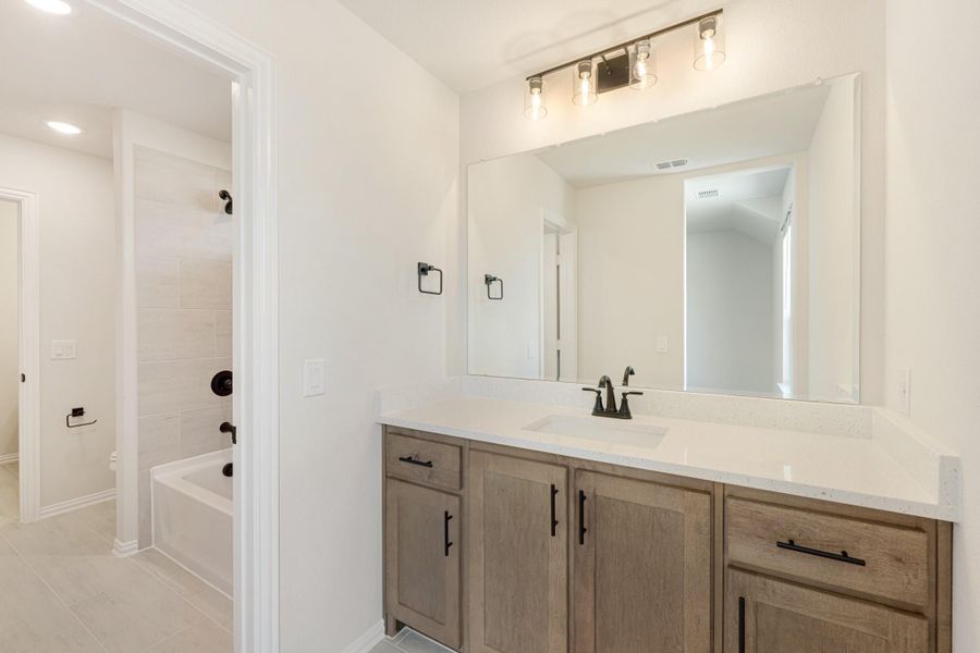 Bathroom with wood vanity, white countertop, large mirror, and separate tub with tile surround Bathroom with wood vanity, white countertop, large mirror, and separate tub with tile surround