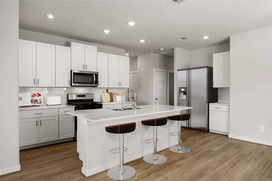 This modern kitchen features sleek white cabinetry, quartz countertops, and stainless steel appliances. A large center island with bar seating and recessed lighting completes the bright, open design, perfect for cooking and entertaining.