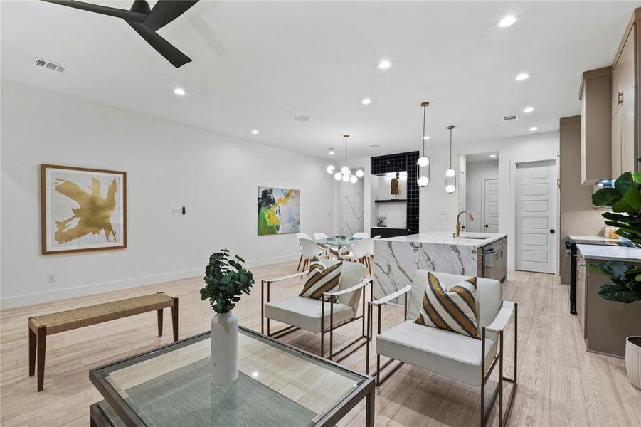 Living room with ceiling fan with notable chandelier and light wood-type flooring