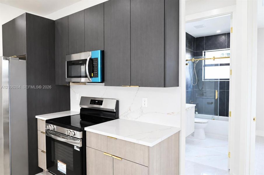 Kitchen featuring flat-panel two-tone cabinetry, quartz countertops, stainless steel appliances, and gold-tone hardware