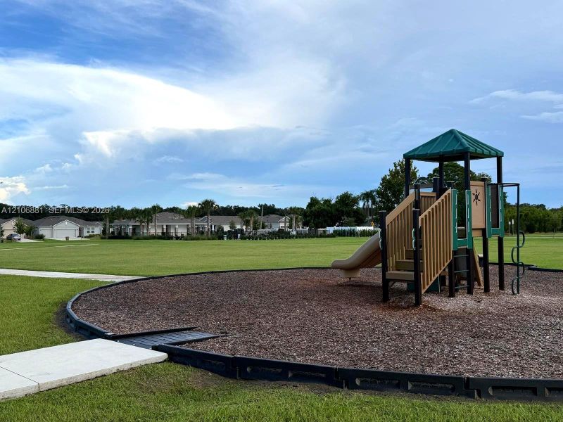 Outdoor recreational area featuring a playground structure with a slide, contained within a mulched border, set on an expansive open lawn