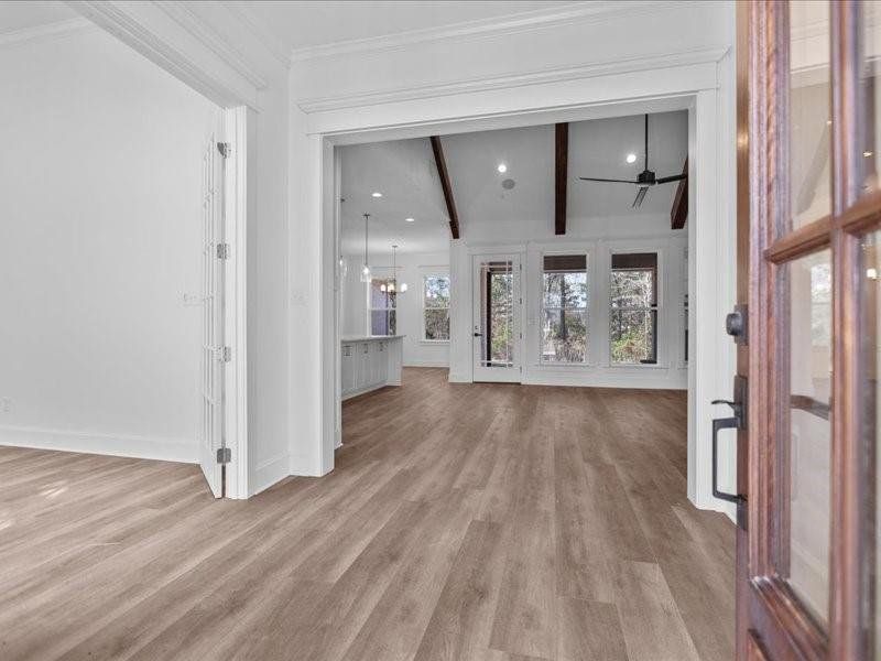 Unfurnished living room with ceiling fan, light wood-style flooring, a chandelier, beamed ceiling, and ornamental molding