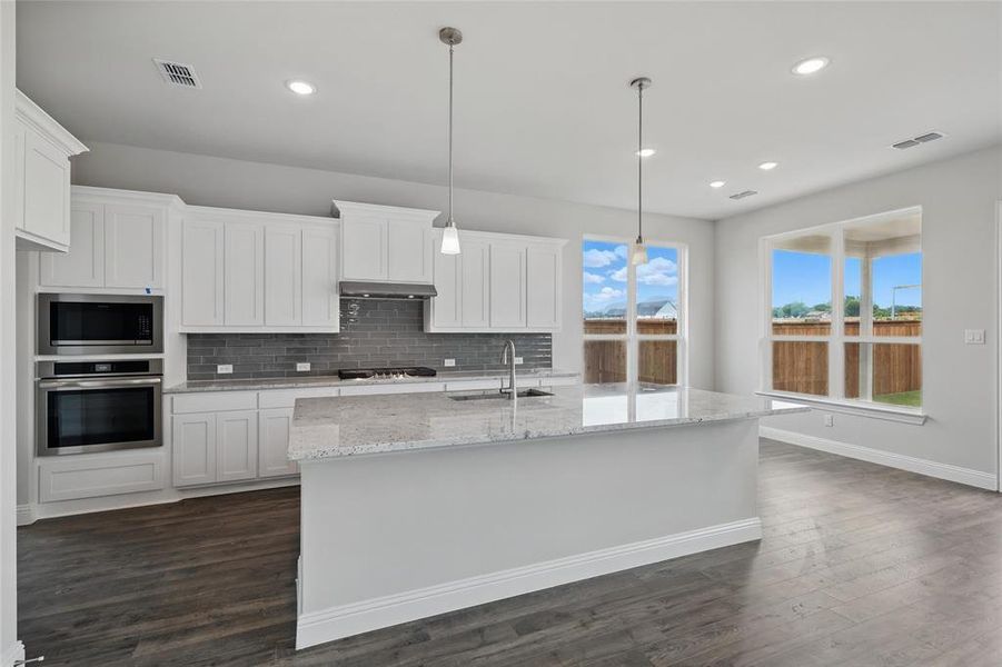 Kitchen featuring stainless steel appliances, a sink, tasteful backsplash, under cabinet range hood, and white cabinets Kitchen featuring stainless steel appliances, a sink, tasteful backsplash, under cabinet range hood, and white cabinets