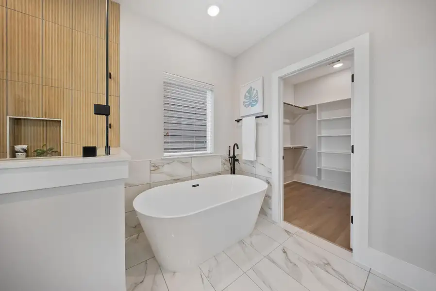 Luxurious master bathroom featuring a sleek freestanding tub, elegant marble tile, and a spacious walk-in closet for ultimate comfort and style.