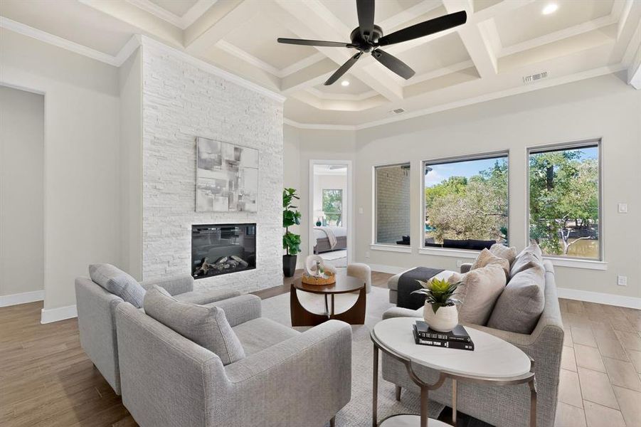 Spacious living area featuring a coffered ceiling, wood-finish flooring, and a contemporary fireplace with a stacked stone surround