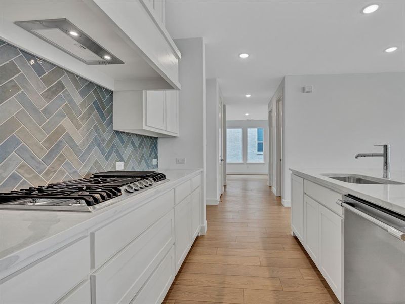 Kitchen featuring stainless steel appliances, sink, light stone countertops, light hardwood / wood-style floors, and backsplash