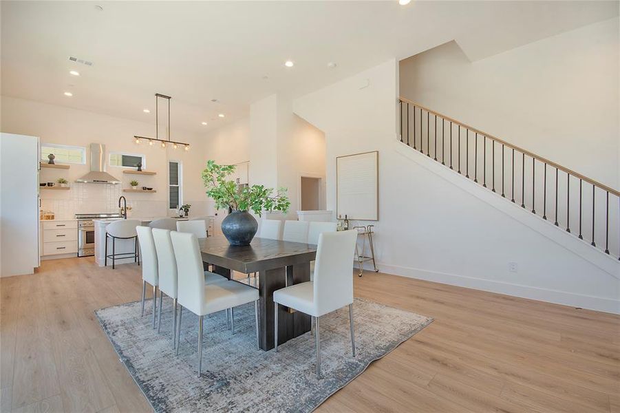 Dining space featuring light wood-style flooring, recessed lighting, stairway, and a high ceiling Dining space featuring light wood-style flooring, recessed lighting, stairway, and a high ceiling