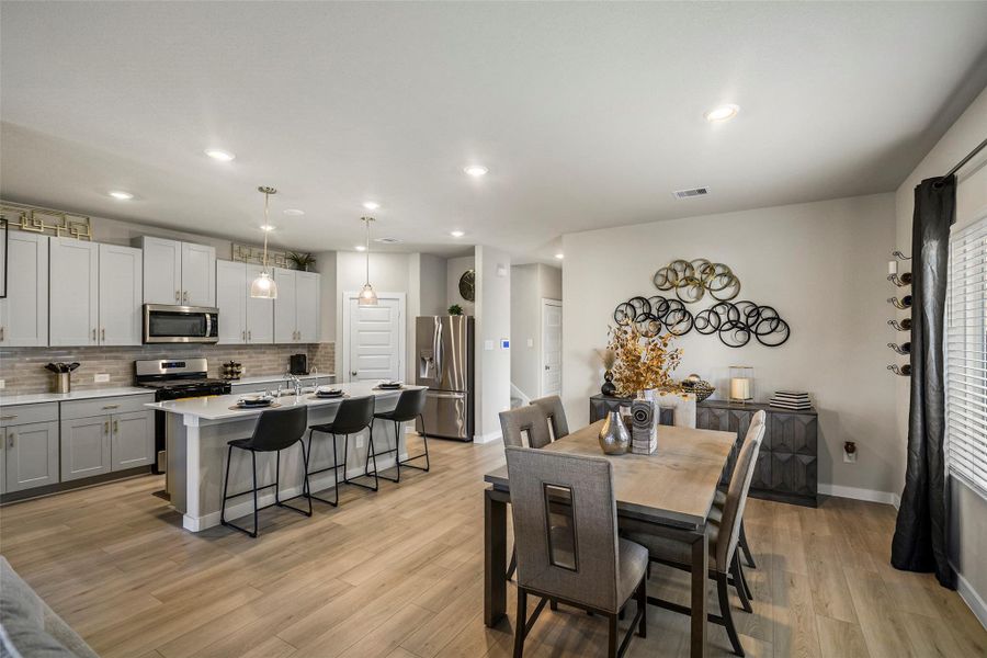 Spacious open-concept kitchen and dining area with modern gray cabinetry, stainless steel appliances, and a stylish island with seating. Perfect for entertaining and family gatherings.