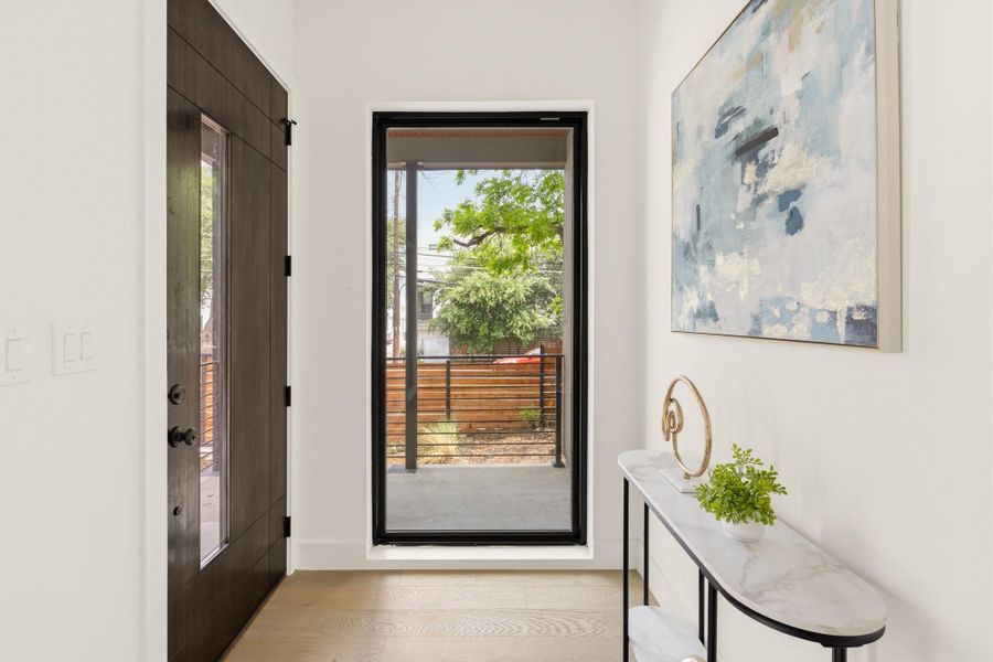 Entryway featuring a dark wood-finish door with glass paneling, light wood-finish flooring, and a floor-to-ceiling window with black trim