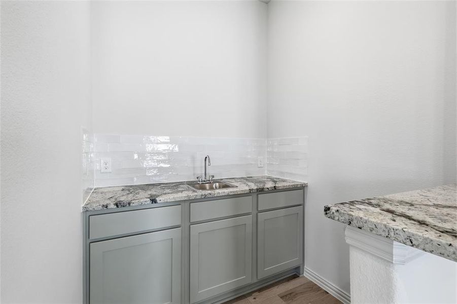 Wet bar featuring gray shaker-style cabinetry, a stainless steel sink with a gooseneck faucet, and a light-toned patterned countertop Wet bar featuring gray shaker-style cabinetry, a stainless steel sink with a gooseneck faucet, and a light-toned patterned countertop