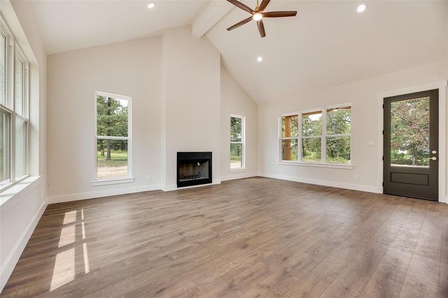 Unfurnished living room featuring high vaulted ceiling, beam ceiling, light wood-style floors, recessed lighting, and ceiling fan