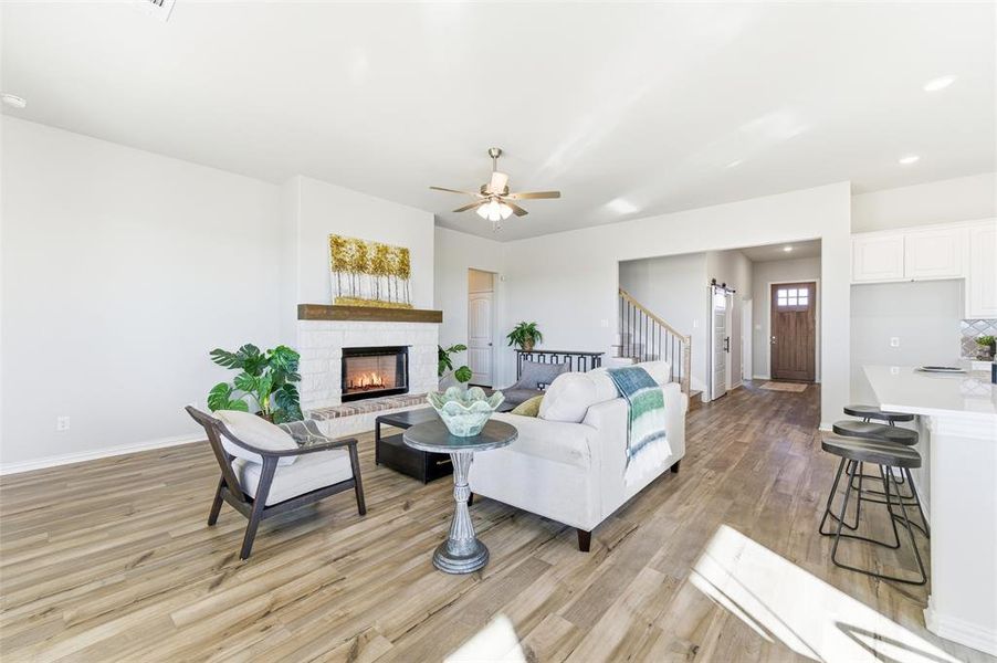 Living area with light wood-style flooring, a brick fireplace, ceiling fan, and stairway