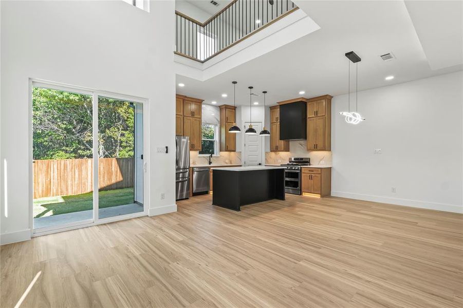 Kitchen with hanging light fixtures, a center island, brown cabinets, appliances with stainless steel finishes, and a high ceiling