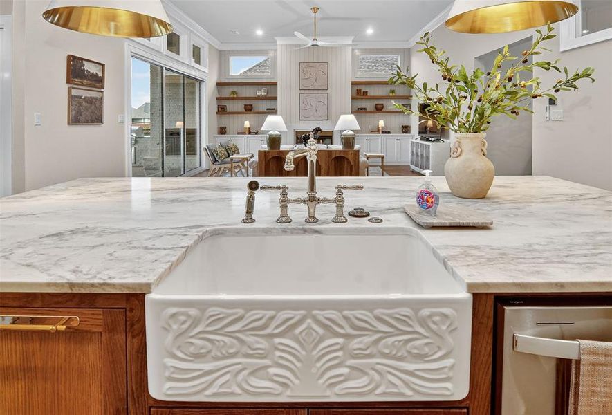 Kitchen featuring hanging light fixtures, stainless steel dishwasher, brown cabinets, a ceiling fan, and a kitchen island with sink
