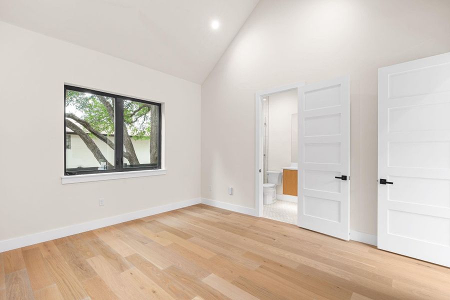 Room featuring high vaulted ceilings, light wood-finish flooring, a modern black-framed window, and crisp white walls