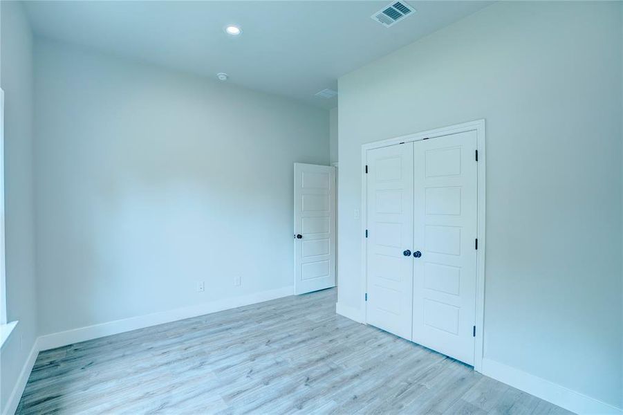 Interior room featuring light-toned walls, wood-finish flooring, recessed lighting, and white bi-fold closet doors with black hardware