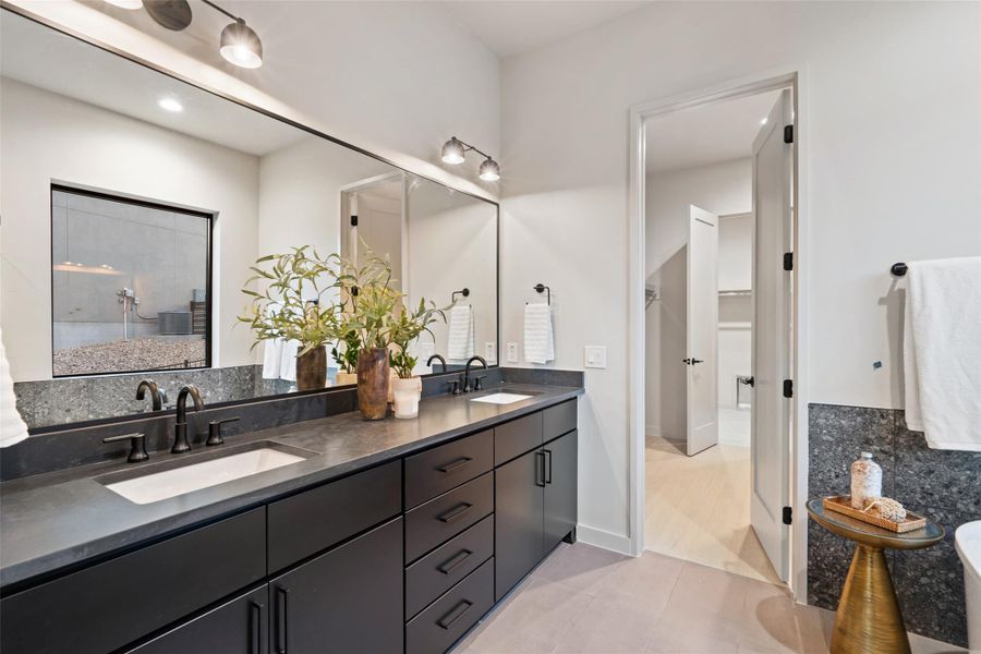 A chic primary bathroom vanity with dual sinks, modern dark cabinetry, and stone counters provides a functional oasis. A chic primary bathroom vanity with dual sinks, modern dark cabinetry, and stone counters provides a functional oasis.