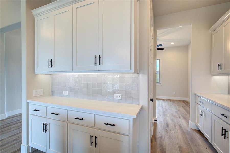 Kitchen with backsplash, white cabinets, ceiling fan, and light hardwood / wood-style floors