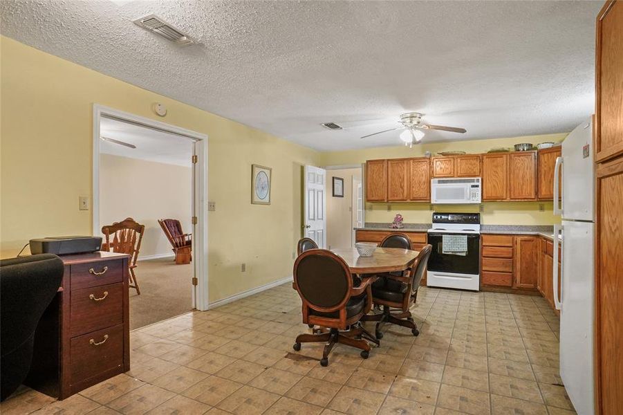 Kitchen with white appliances, ceiling fan, brown cabinetry, a textured ceiling, and light countertops