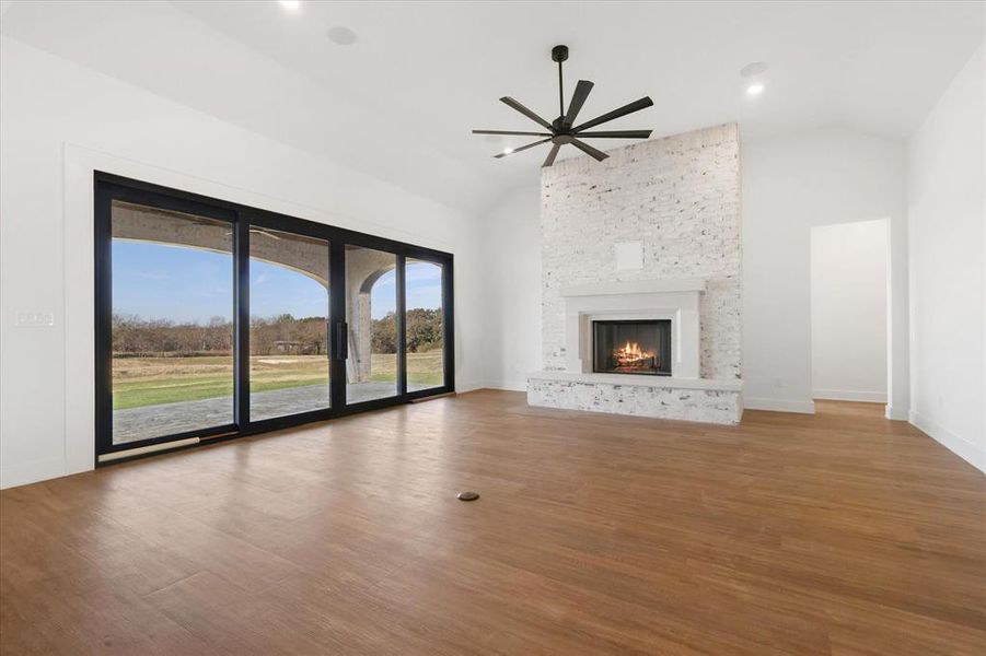 Unfurnished living room with vaulted ceiling, a stone fireplace, light wood finished floors, and ceiling fan