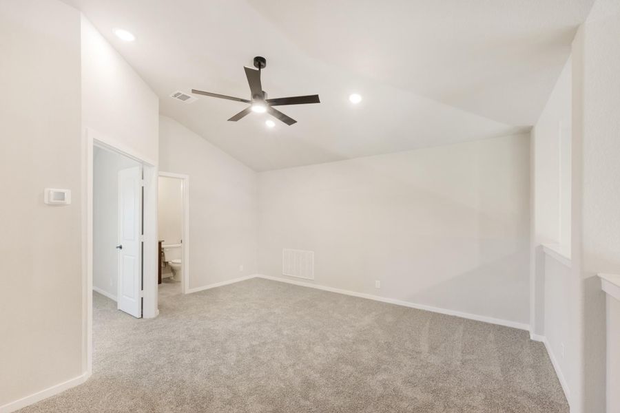 Empty bedroom with vaulted ceiling, ceiling fan, carpet flooring, and attached bathroom doorway