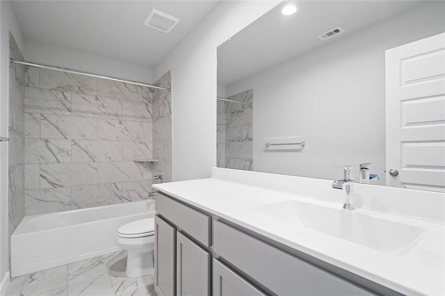 Secondary bath features tile flooring, bath/shower combo with tile surround, wood cabinets, beautiful light countertops, mirror, sleek fixtures and modern finishes!