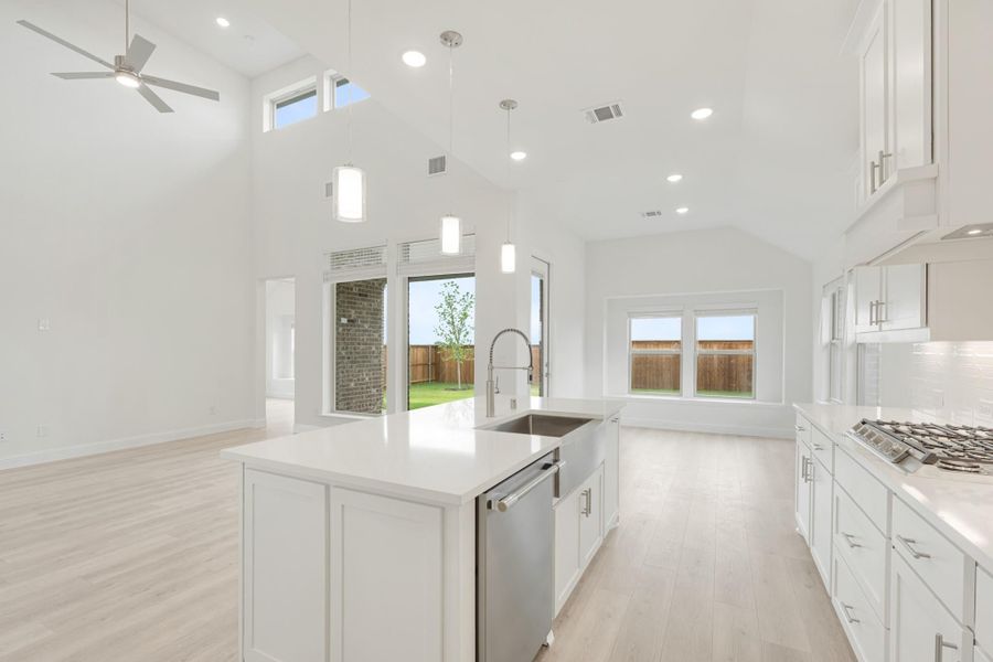 Open kitchen with white cabinets, large island, vaulted ceiling, and light wood floors open to living area
