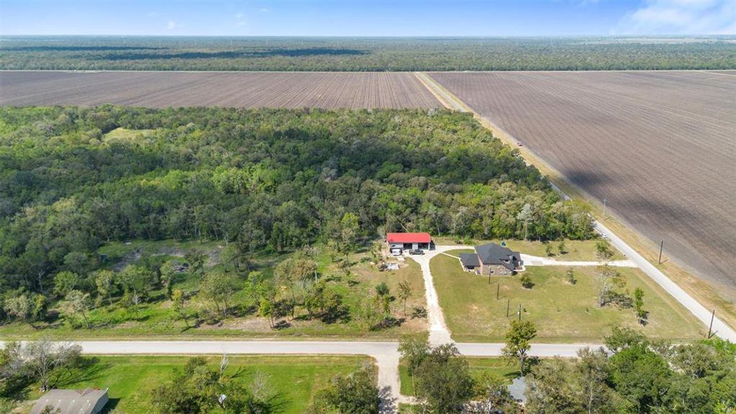 This photo showcases a rural property featuring a spacious home with a large yard, bordered by lush woods and expansive farmland. The house is accessible via a long driveway, offering privacy and a serene setting.