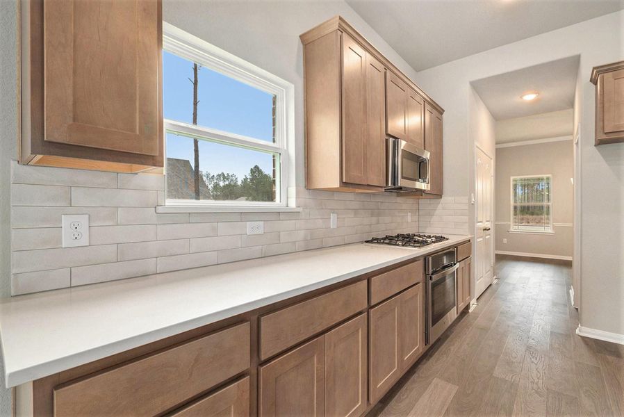 This kitchen features modern wood cabinetry, a sleek gas stove, and stainless steel appliances. The light countertops and subway tile backsplash add a bright, contemporary feel, with ample natural light from the window.