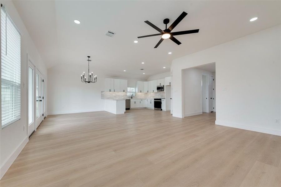 Unfurnished living room with lofted ceiling, ceiling fan with notable chandelier, and light wood-type flooring