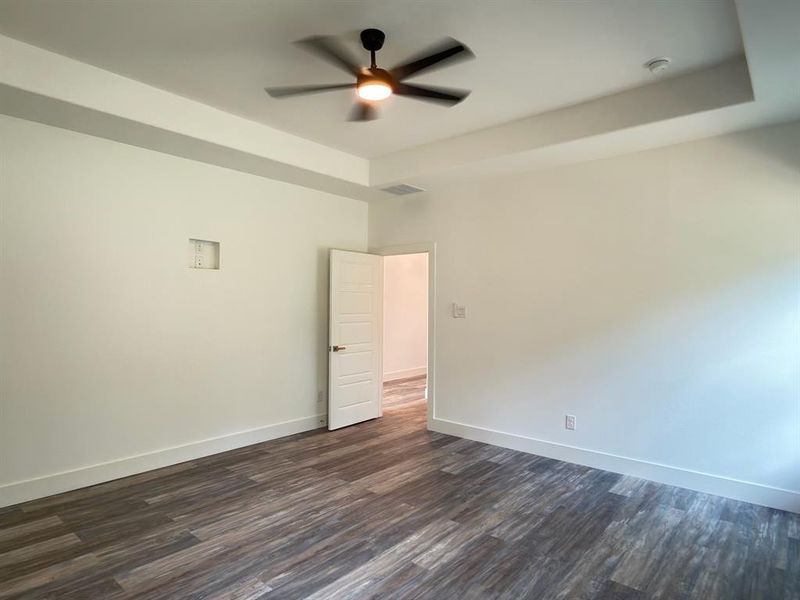 Room featuring a tray ceiling with a ceiling fan, wood-finish flooring, white baseboards, and a white interior door