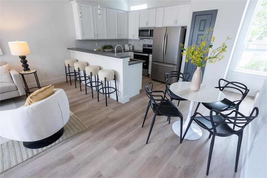 Kitchen with white cabinets, light hardwood / wood-style flooring, tasteful backsplash, kitchen peninsula, and stainless steel appliances