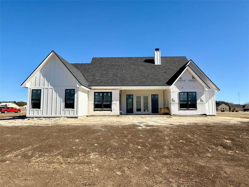 Rear view of house featuring french doors, board and batten siding, a chimney, and a shingled roof