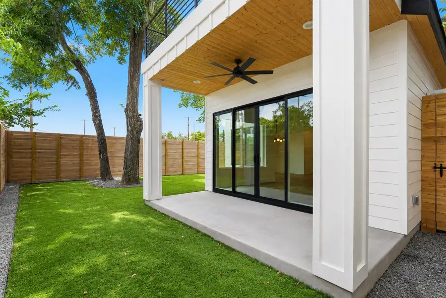 An inviting concrete patio opens to a vibrant green lawn, framed by a handsome wooden fence.