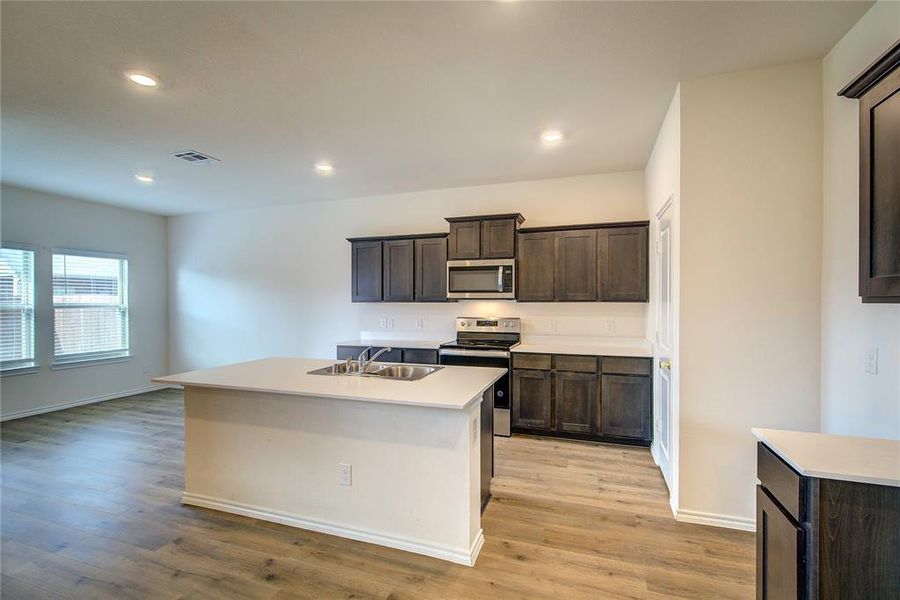 Kitchen featuring stainless steel appliances, dark brown cabinets, an island with sink, light wood-style flooring, and recessed lighting