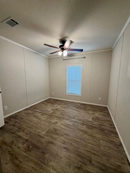Room featuring wood-finish flooring, a ceiling fan with integrated lighting, window with blinds, and neutral wall paneling