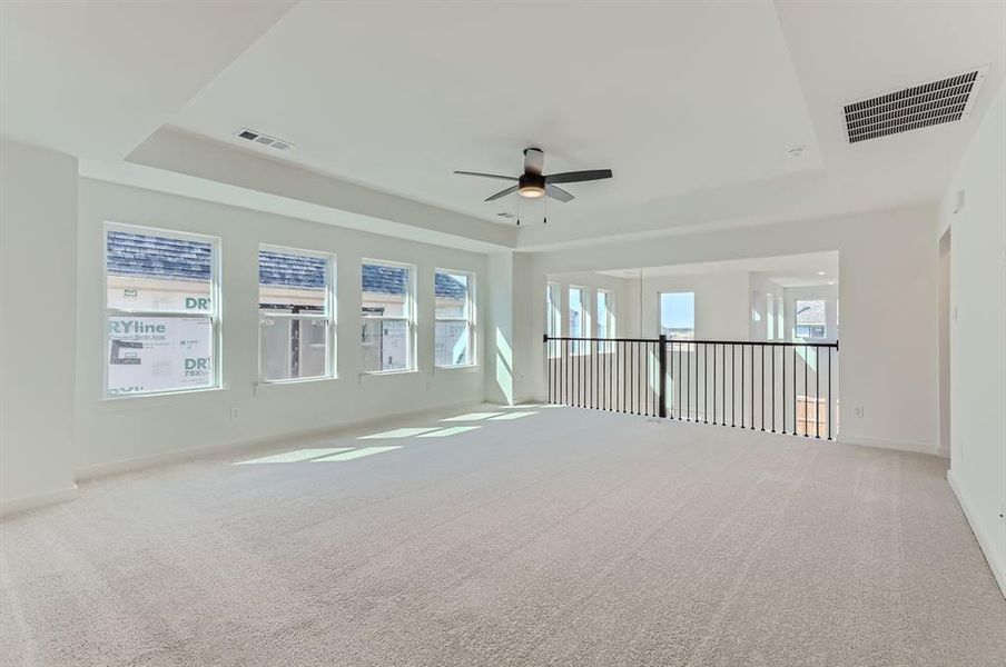 Empty room with a raised ceiling, carpet floors, and ceiling fan