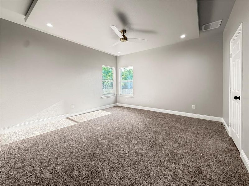 Spacious interior room featuring a tray ceiling with recessed lighting, a ceiling fan, and two windows providing natural illumination