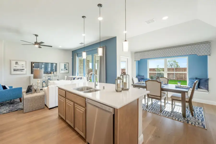 Open-concept kitchen with island, pendant lights, and views into dining and living areas with hardwood floors