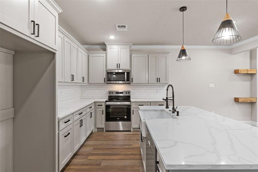 Kitchen with ornamental molding, dark hardwood / wood-style flooring, appliances with stainless steel finishes, light stone counters, and hanging light fixtures