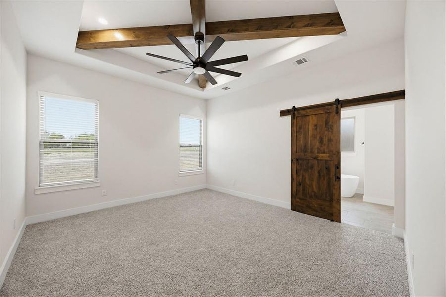 Spacious room featuring a tray ceiling with wood-finish beams, a modern ceiling fan, two windows, and a barn door