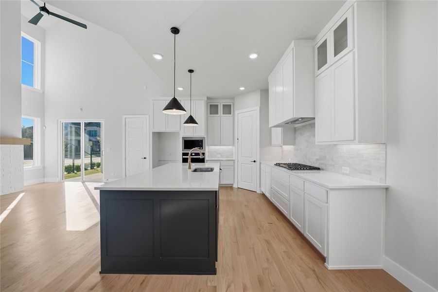 Kitchen featuring glass insert cabinets, white cabinetry, decorative backsplash, light wood-style flooring, and a center island with sink