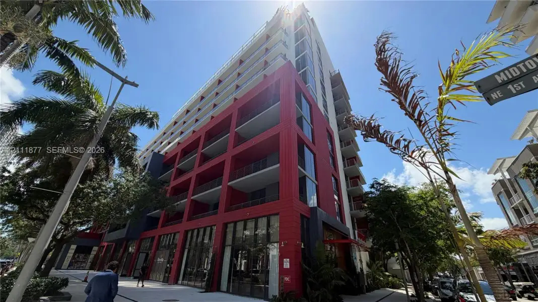 High-rise building exterior featuring a red-accented concrete facade, expansive glass windows, and private balconies on multiple levels