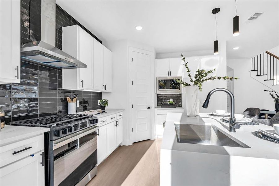 Kitchen featuring backsplash, stainless steel appliances, wall chimney range hood, light hardwood / wood-style floors, and hanging light fixtures