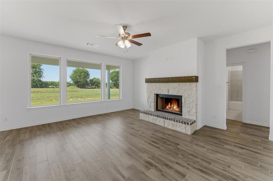 Spacious interior featuring wood-finish flooring, a stone-clad fireplace with a brick hearth and wood mantel, and a ceiling fan
