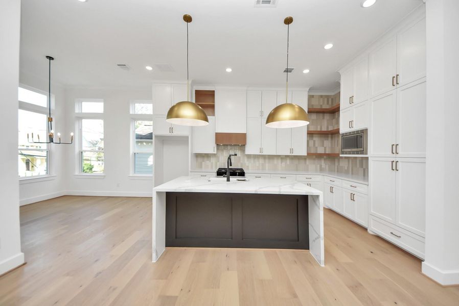 A modern kitchen highlighted by crisp white cabinetry, a statement marble island, and elegant gold pendant lighting. Multiple windows flood the space with natural light, while light wood flooring adds warmth and balance to the clean, contemporary design.