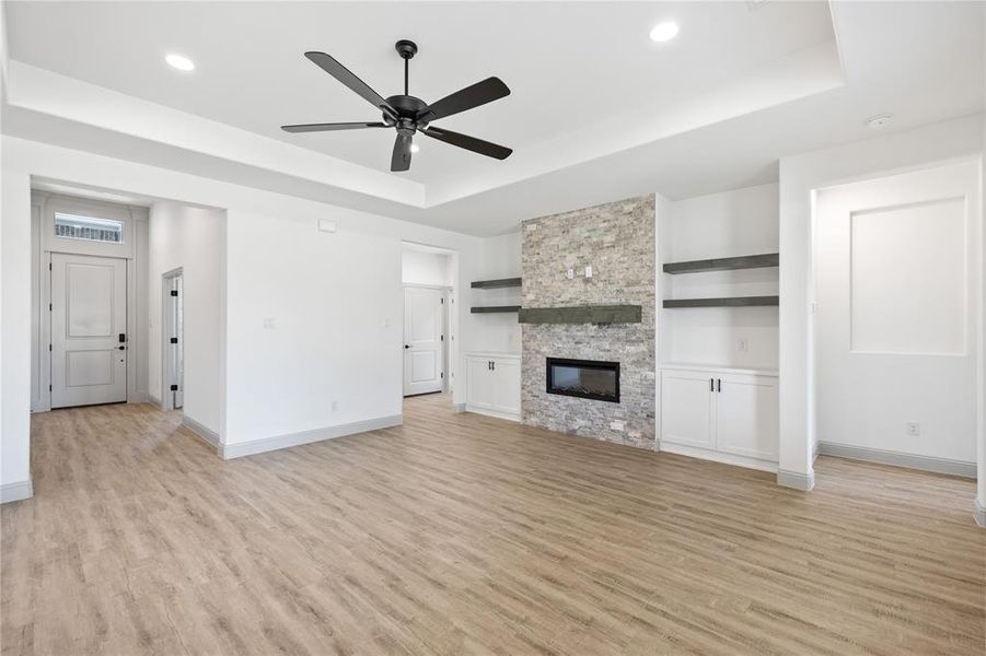 Unfurnished living room featuring light wood-style floors, a raised ceiling, and a stone fireplace