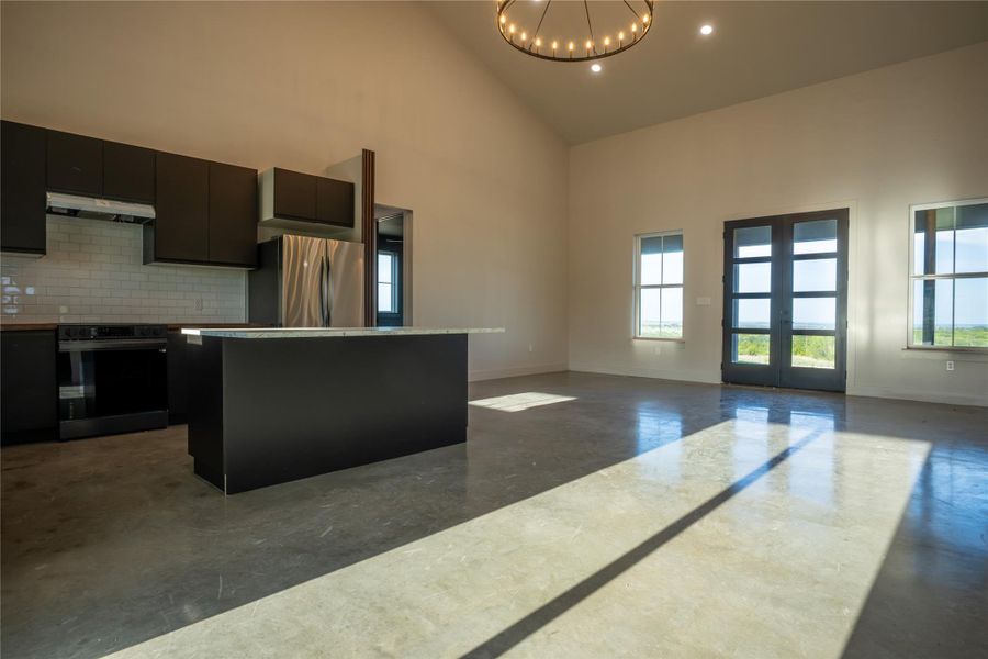 Kitchen featuring plenty of natural light, a kitchen island, finished concrete floors, freestanding refrigerator, and high vaulted ceiling
