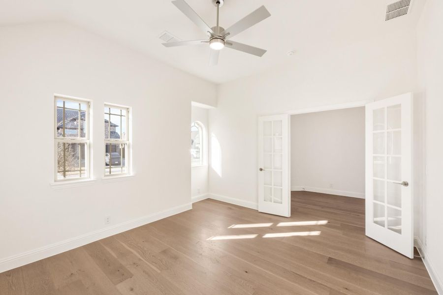 Empty room with hardwood floors, ceiling fan, white walls, and French doors leading to adjacent space Empty room with hardwood floors, ceiling fan, white walls, and French doors leading to adjacent space