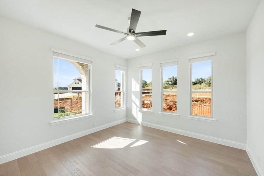Empty bedroom with hardwood floors, ceiling fan, and four windows overlooking a construction site